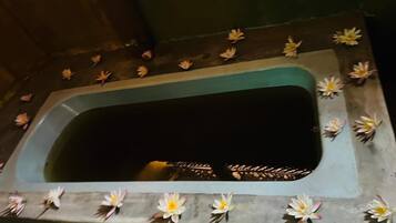 A rectangular bathtub with a dark interior, surrounded by a border decorated with artificial water lilies.