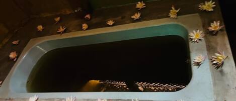 Una bañera rectangular con el interior oscuro, rodeada por un borde decorado con nenúfares artificiales.