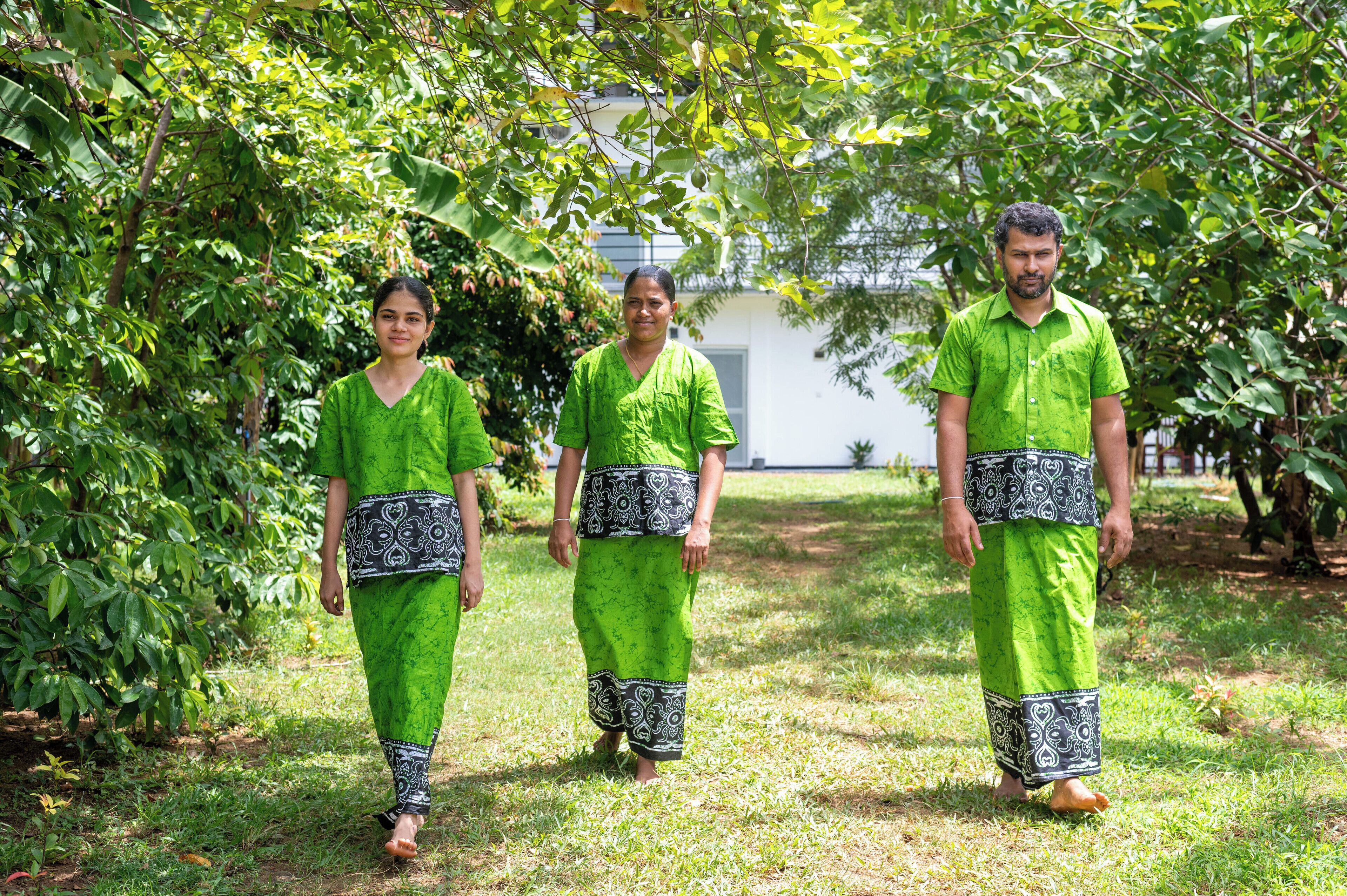 Three individuals in green traditional attire walking on a grassy path.