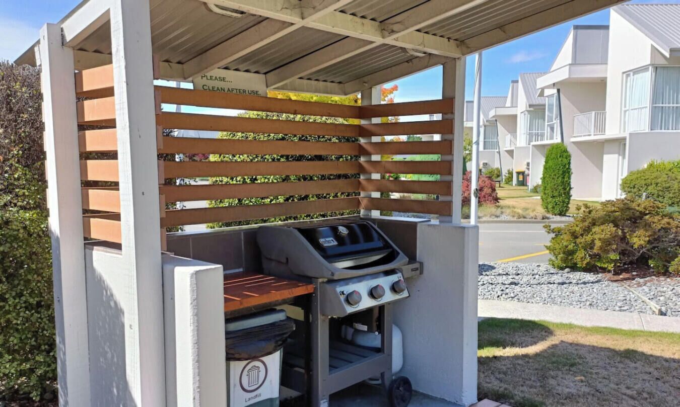 A barbecue grill under a covered structure with a sign instructing to clean after use.