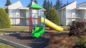 Leikkikentällä on liukumäki ja kiipeilyteline, ja sen ympärillä on maisemoitu puutarha sekä taustalla asuinkerrostaloja.