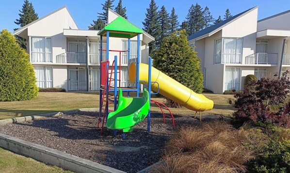 A playground with a slide and climbing structure, surrounded by a landscaped garden and residential buildings in the background. - Mt Hutt Views at 23 Methven (Methven)