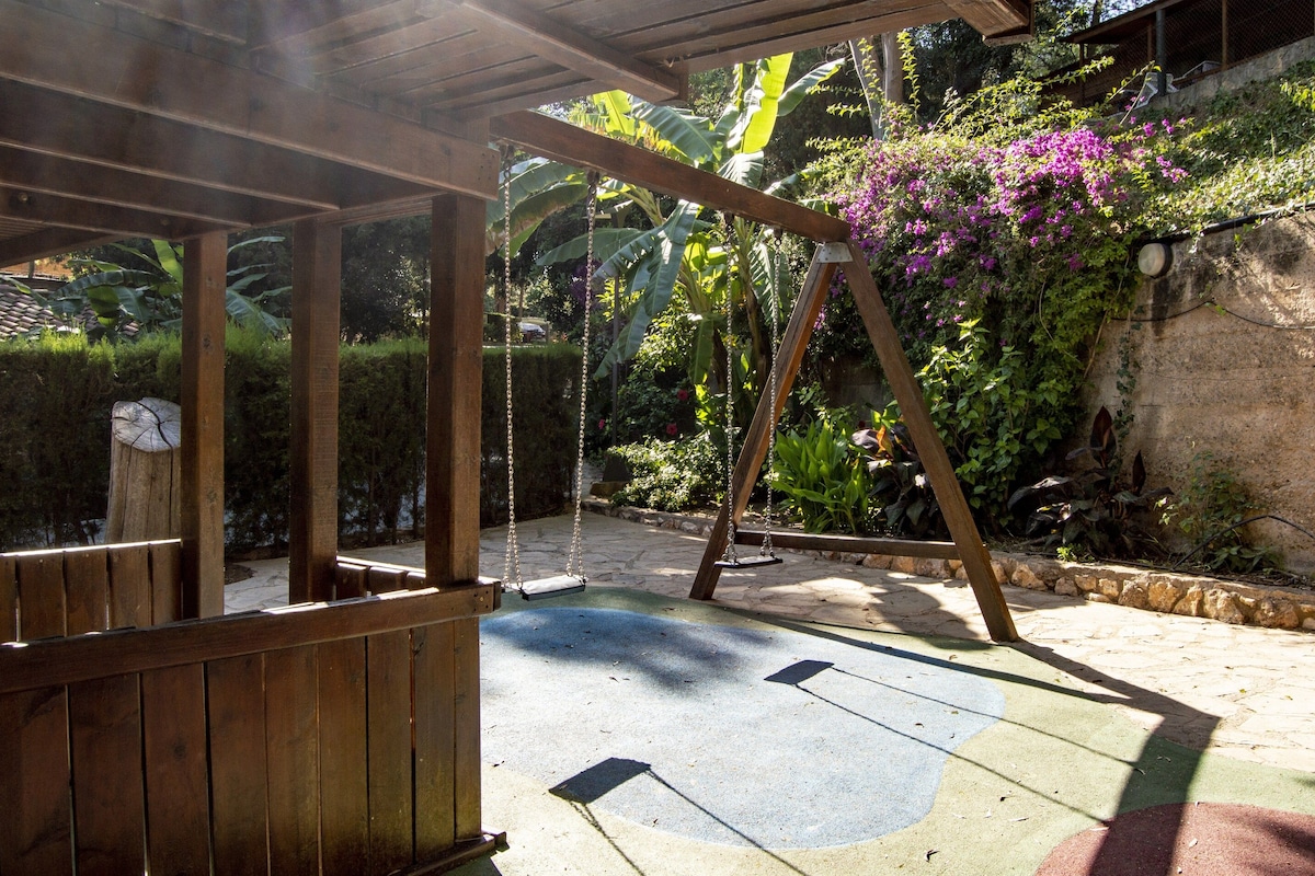 A wooden swing set in a garden with a stone wall and lush vegetation.