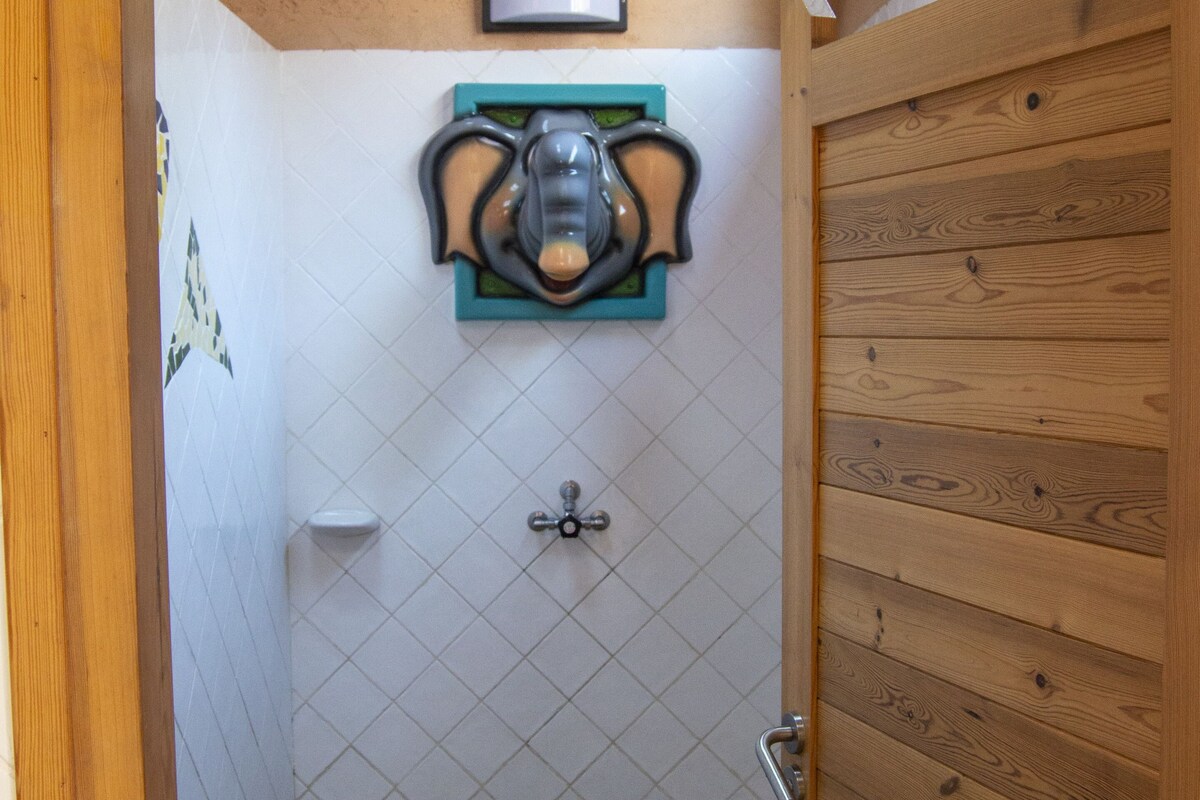 Un baño con puerta de madera, zona de ducha con azulejos y un inodoro fijado a la pared.