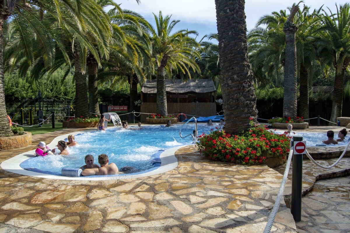 Un espace piscine doté de plusieurs bains à remous et, au fond, d’une structure surmontée d’un toit de chaume.