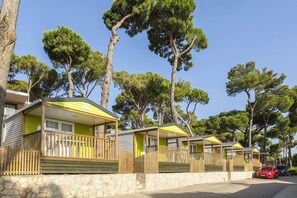 A row of mobile homes with wooden railings, a stone wall, and trees in the background. - Nice Fully Equipped Bungalow (Pals)
