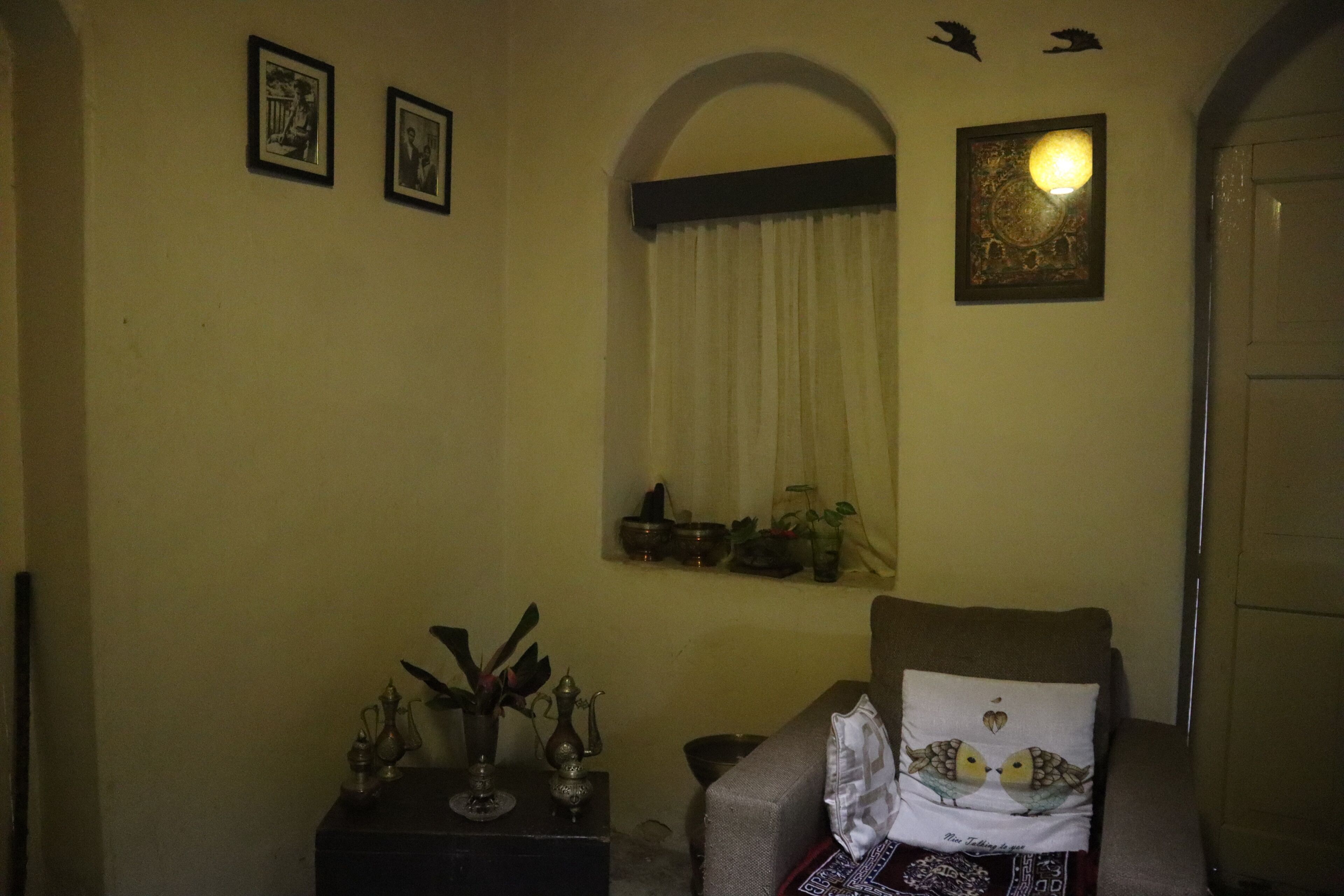 A room with a sofa, a small table with decorative items, a window with curtains, and wall-mounted pictures.