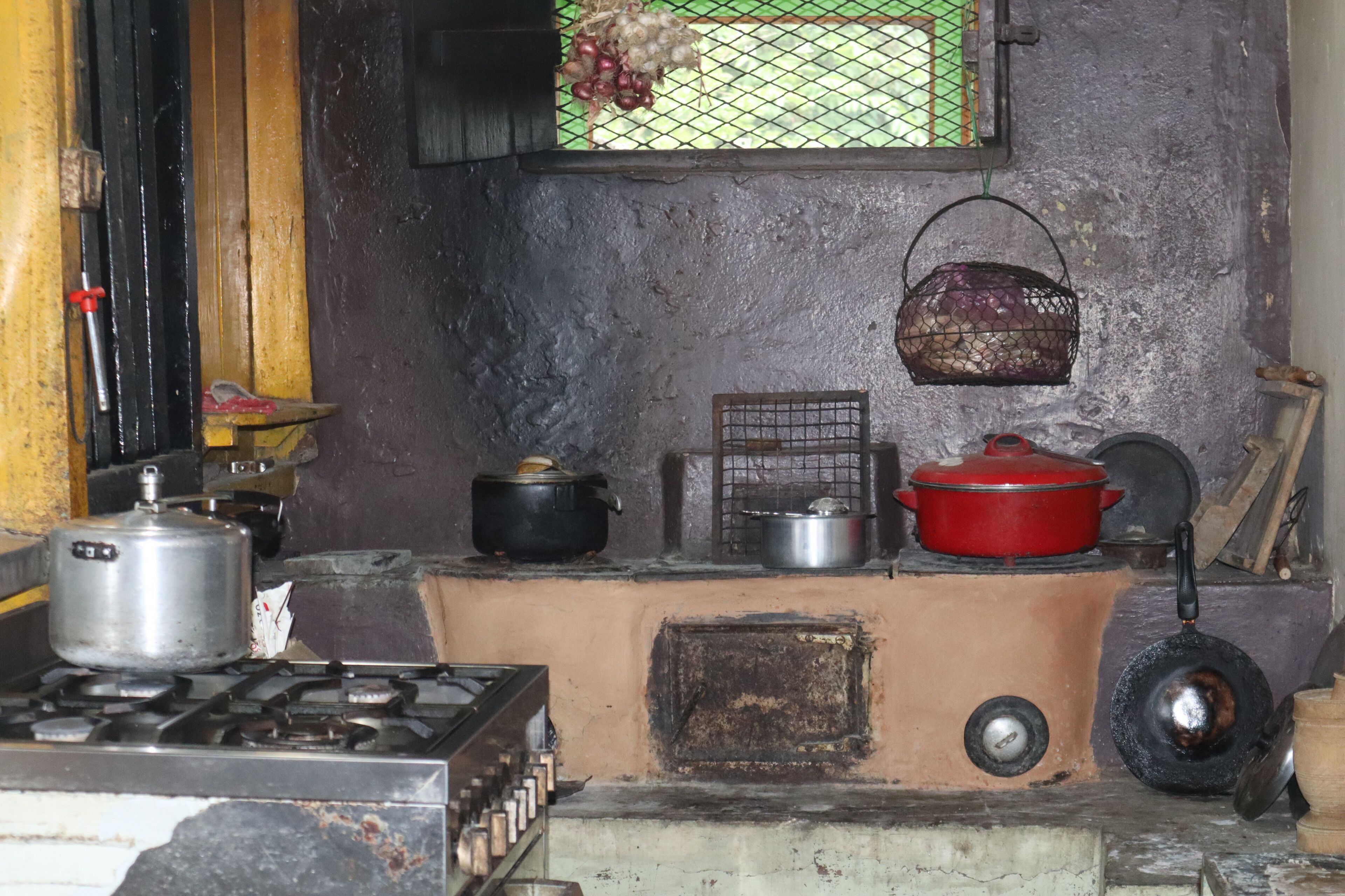 Una cocina rústica con estufa a gas, ollas, una olla roja y una cesta colgante.