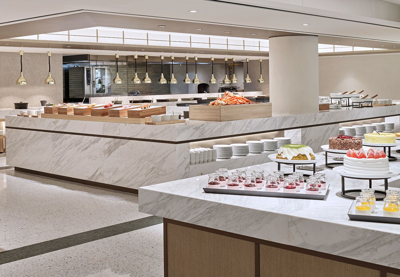 A modern buffet setup with marble counters, a variety of food items, and hanging pendant lights.