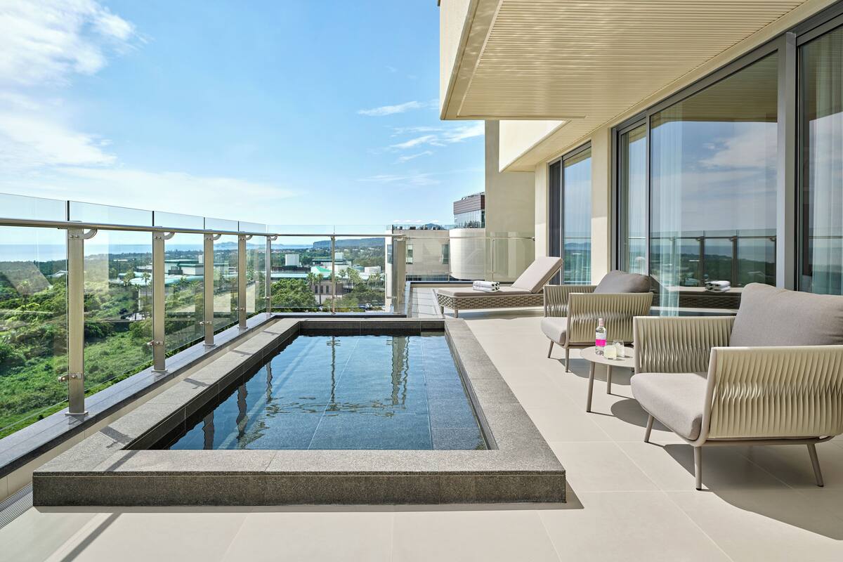 Un espace piscine moderne aménagé sur le toit, offrant une vue dégagée sur le paysage urbain, et doté de chaises longues et d’une petite table.