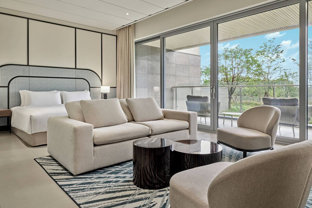 Une chambre d’hôtel moderne dotée d’un grand lit, d’un canapé, d’une table basse et d’un balcon aménagé avec du mobilier d’extérieur.