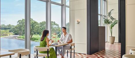 A modern hotel lobby with large windows, a geometric patterned floor, and a view of a water body.