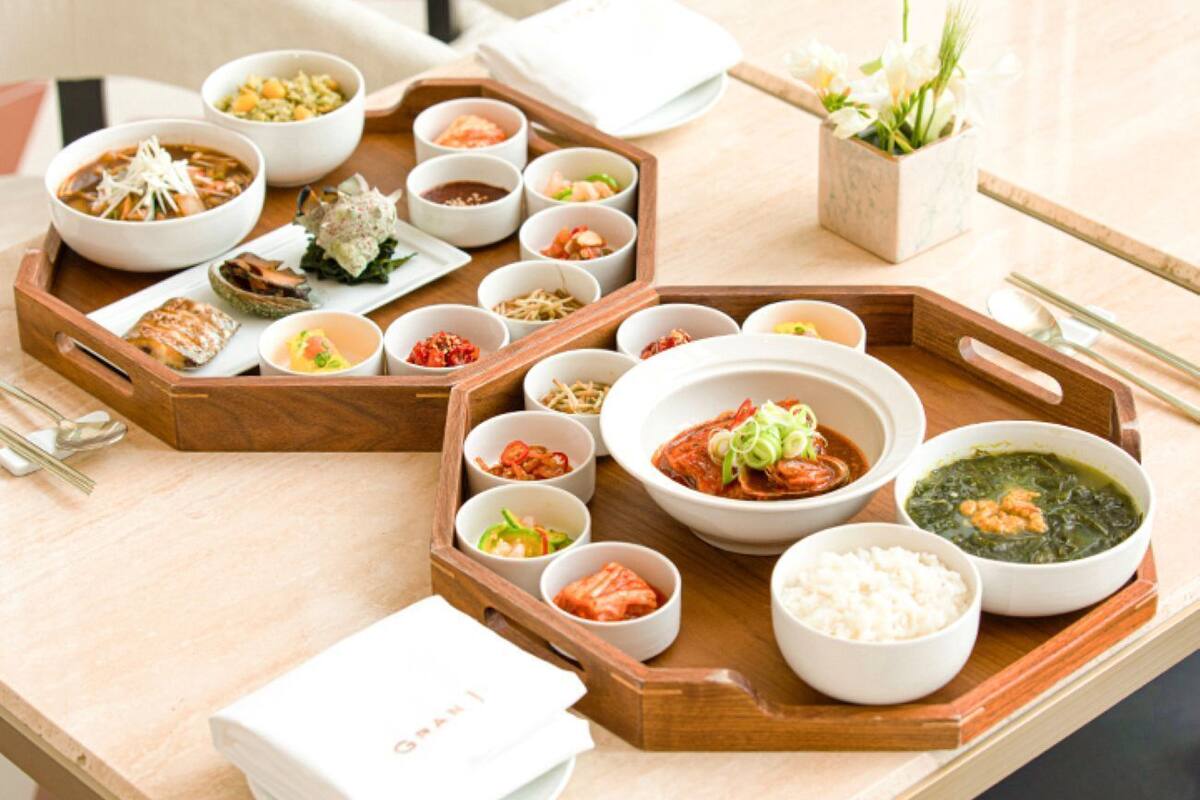 Un plateau en bois contenant divers plats coréens, notamment du kimchi, du riz et de la soupe, est posé sur une table.