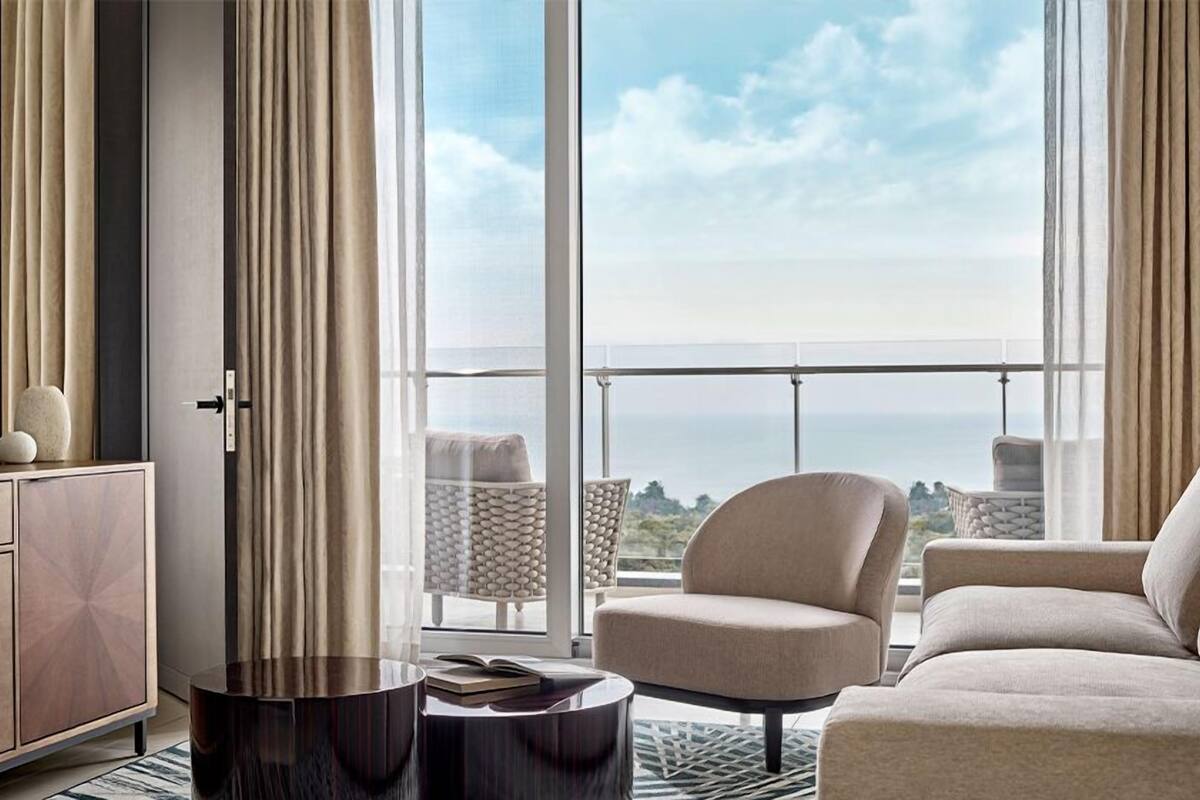 Un salon moderne avec un canapé, un fauteuil et une petite table ronde. Une grande fenêtre offre une vue sur la mer.