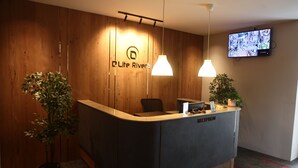 A reception desk with a wooden backdrop, a television mounted on the wall, and two pendant lights. - Dlite Rivera  (Bengaluru)