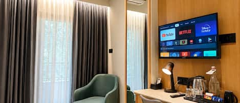 A hotel room with a desk, chair, TV, and curtains.