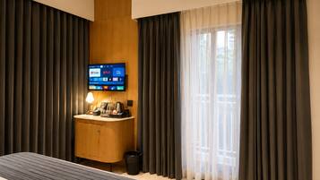 Una habitación de hotel con una cama, un escritorio con lámpara, un televisor mostrando servicios de transmisión y una ventana con cortinas.