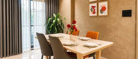 A dining area with a table set for four, chairs, a vase with flowers, and framed artwork on the wall.