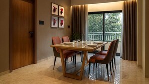 A dining area with a wooden table and chairs, framed artwork on the wall, and a view of greenery outside. - Dlite Rivera  (Bengaluru)