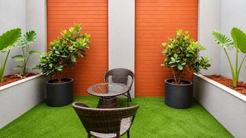 Un pequeño patio con césped artificial, una mesa y una silla de mimbre y plantas en macetas.