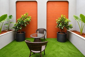 A small patio area with artificial grass, a wicker table and chair, and potted plants. - Dlite Rivera  (Bengaluru)