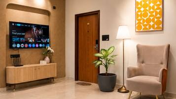 Un hall de hotel con un televisor de pantalla plana, una consola de madera, una planta en maceta, una lámpara y una obra de arte enmarcada.