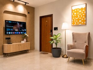 A hotel lobby with a flat-screen TV, a wooden console, a potted plant, a lamp, and a framed artwork. - Dlite Rivera  (Bengaluru)