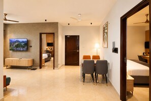 A hotel room with a bed, a desk, a TV, and a dining area with chairs. - Dlite Rivera  (Bengaluru)