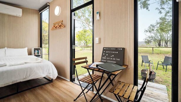 Una camera moderna con un letto, una scrivania con un portatile, una sedia e vista sull'esterno.