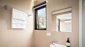 Un bagno con il water, un lavandino, un portascopevoli, una finestra e uno specchio.