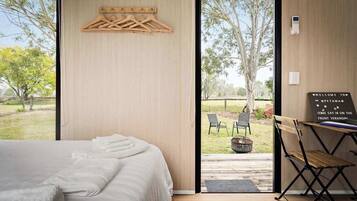 Ein modernes Schlafzimmer mit einem großen Bett, einem Wäscheständer aus Holz und Blick ins Freie.