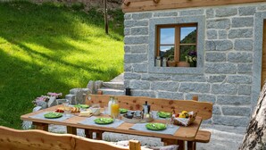 Un bâtiment en pierre avec une table en bois dressée pour le petit-déjeuner, entouré de verdure.
