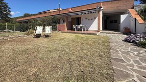 Un edificio a due piani con tetto in tegole, una veranda coperta con posti a sedere all'aperto e un vialetto in pietra che conduce all'ingresso.