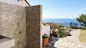 Un muro esterno in pietra con una porta, una pianta in vaso e vista sul mare.