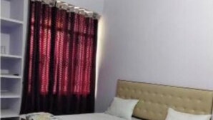 A bedroom with a bed, a ceiling fan, a wardrobe, and a window with curtains. - Hotel Mahadev inn (Varanasi)