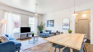 A modern living room with a wooden dining table, sofas, a TV, and a large window. - Le Plateau Apartment & Suite Near Mont-Royal Ave (Montréal)