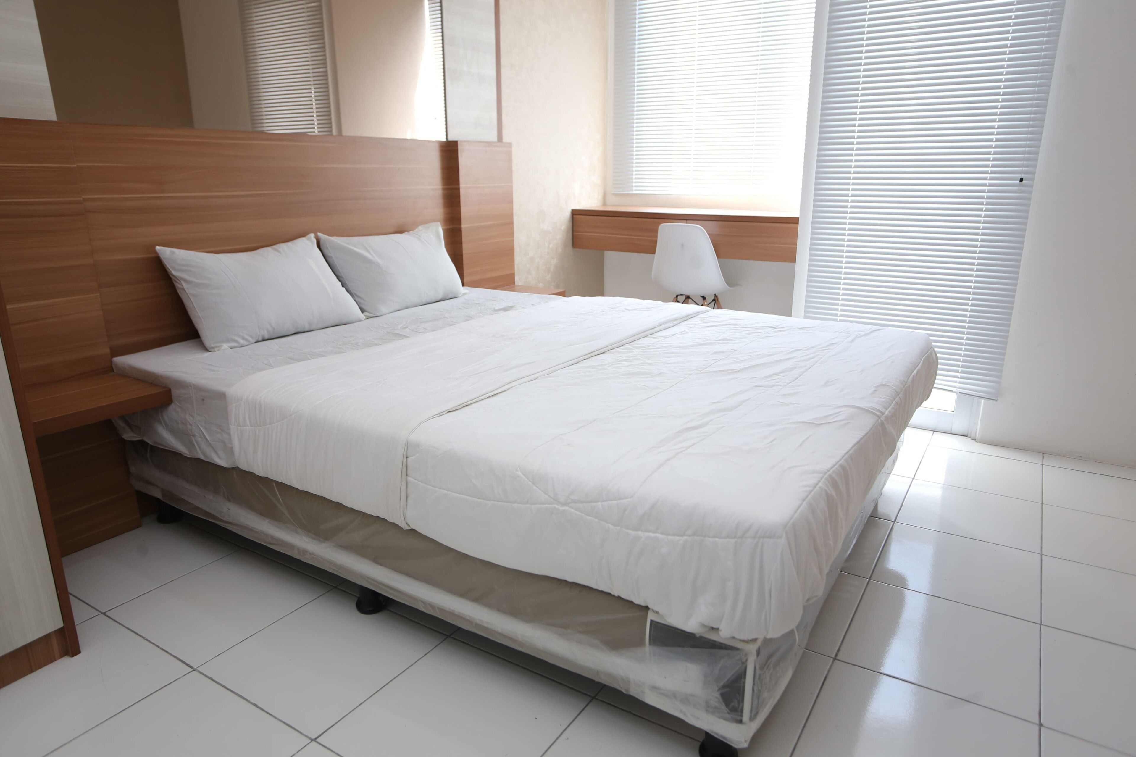 A neatly made bed with a wooden headboard, a bedside table, and a window with blinds.