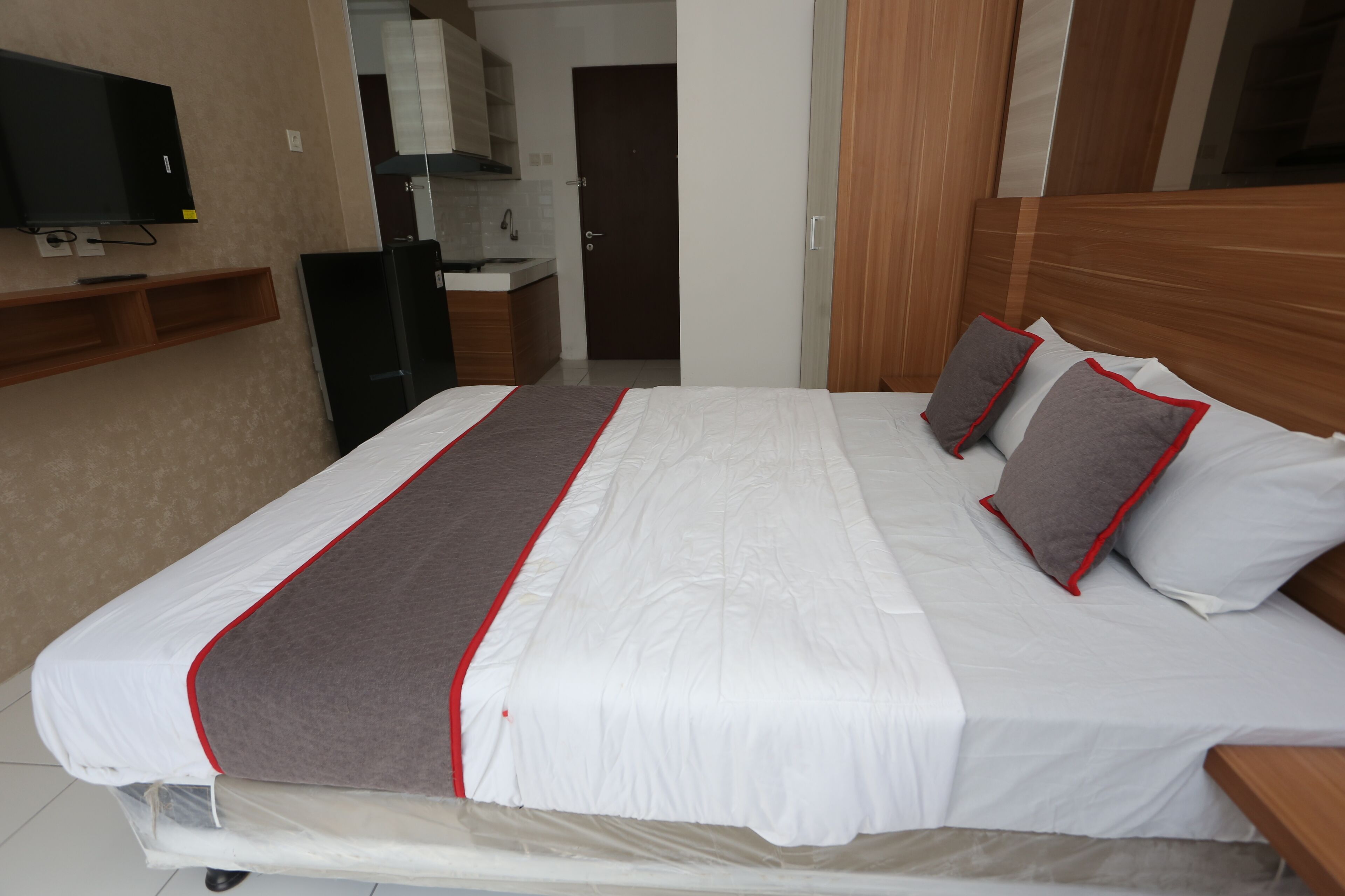 Una cama bien hecha con una colcha blanca y gris, un cabecero de madera y dos almohadas con detalles rojos.