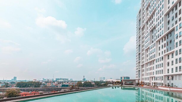 A high-rise building with a large swimming pool in the foreground. - Collection O metroploitian park Serviced Apartmen (Bekasi)