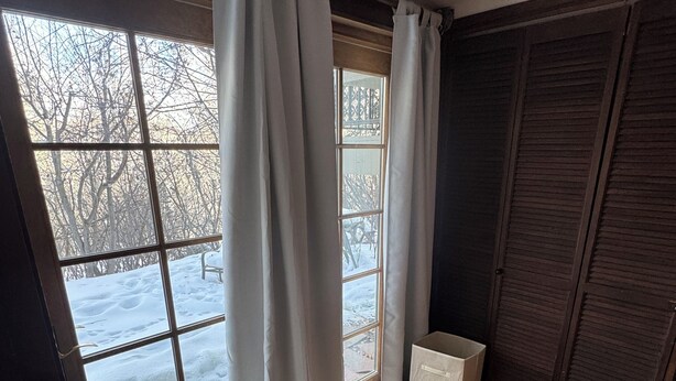 Ein Zimmer mit großem Fenster, einer Holztür und einem Fliesenboden.