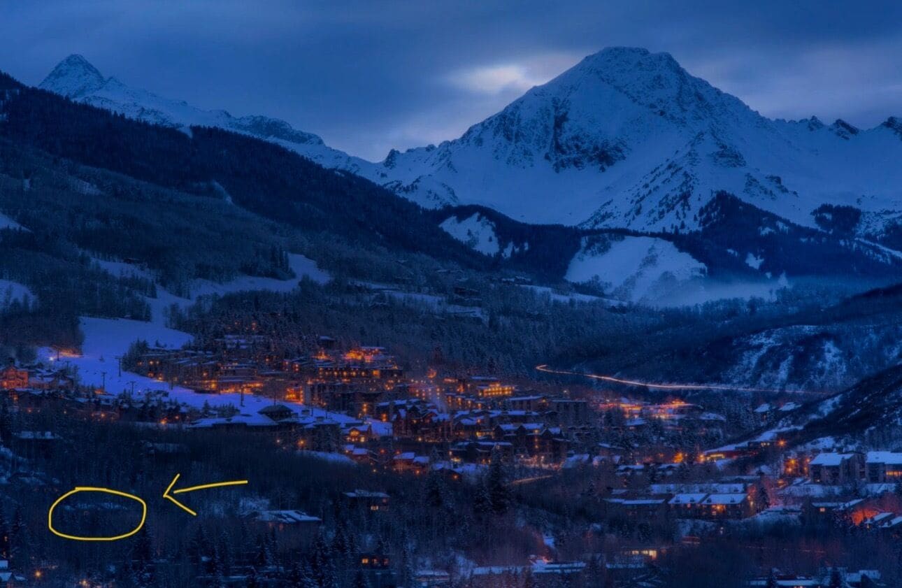 A snow-covered mountain town at dusk with illuminated buildings and a winding road.