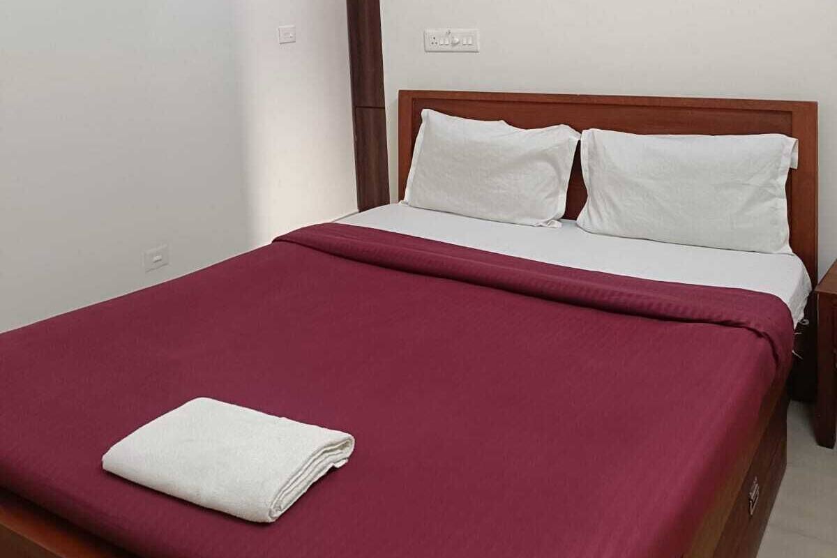 A neatly made bed with a red bedspread and white pillows, a wooden headboard, and a small bedside table with a lamp.