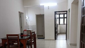 Egy tágas szoba, melyben egy étkezősarok található, egy faasztallal és -székekkel, egy kis székkel, valamint csempézett padlóval.