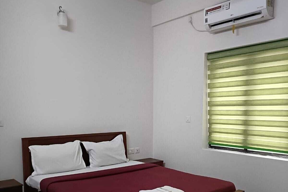 A bedroom with a single bed, a nightstand, a wall-mounted air conditioner, and a window with blinds.