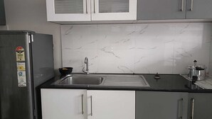 Egy konyha, amelyben rozsdamentes acél hűtőszekrény, csaptelepes mosogató és fogantyús szekrények találhatók.