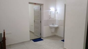 A narrow hallway with a white door, a white sink, and a mirror on the wall.