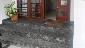 Egy üvegpanelekkel ellátott, fából készült ajtó, egy virágtartóban lévő növény és egy csempézett bejárat.