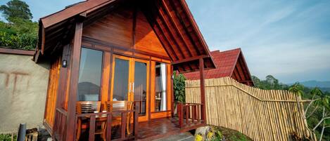 A wooden house with a porch, large windows, and a view of the surrounding landscape.