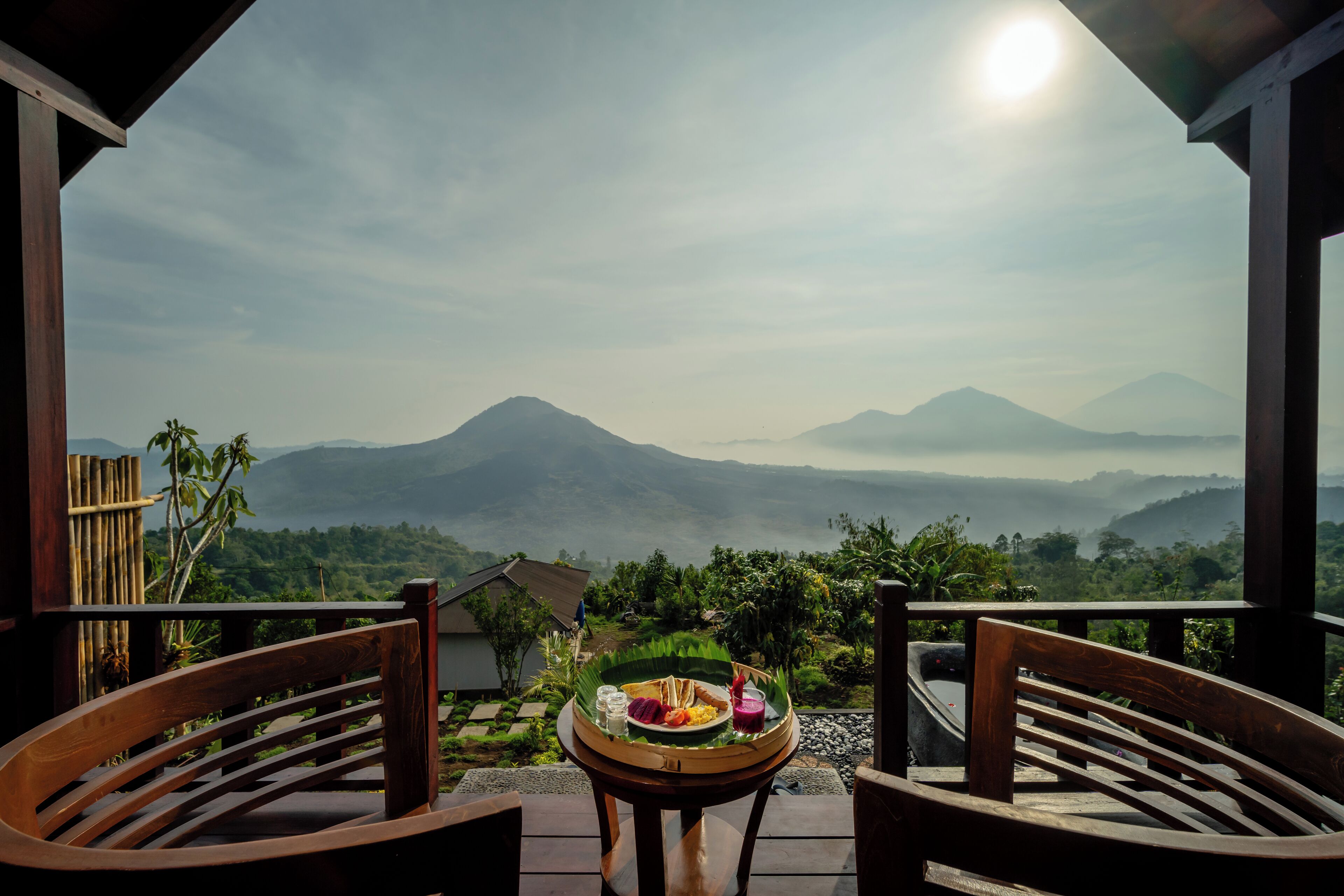 A wooden table with a tray of food and a glass of drink, overlooking a mountainous landscape.