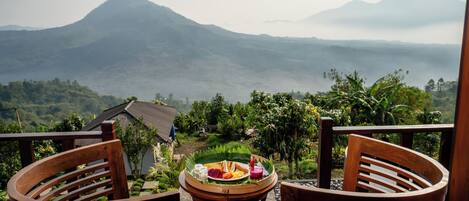 A wooden table with a tray of food and two chairs on a balcony overlooking a mountainous landscape.